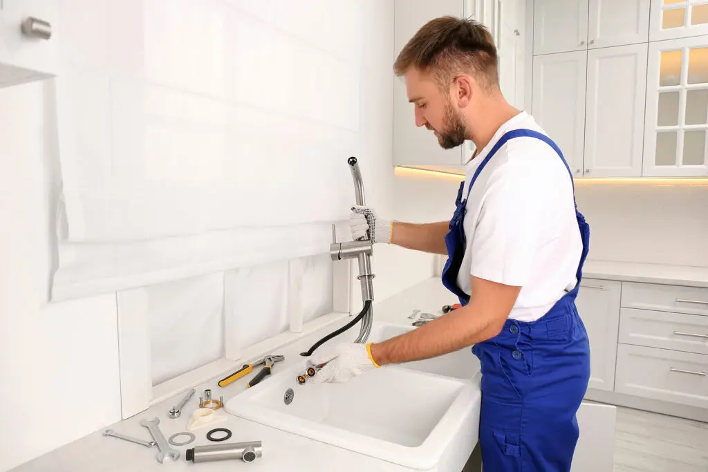 Professional plumber repairing water tap in kitchen
