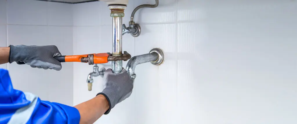 Technician plumber using a wrench to repair a water pipe under t