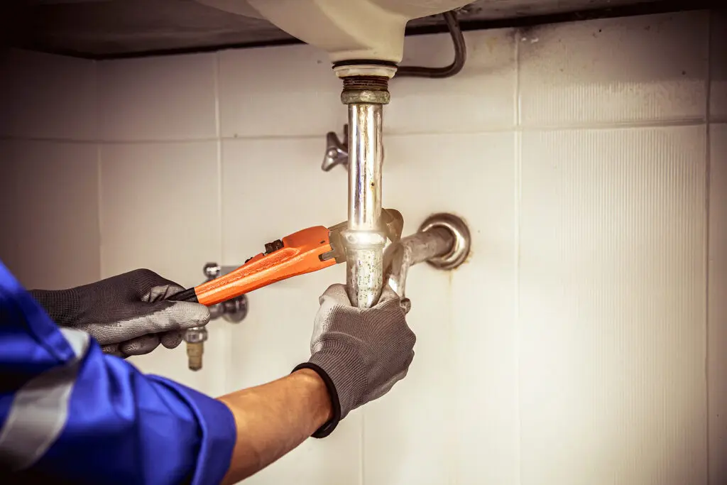 Technician plumber using a wrench to repair a water pipe under t