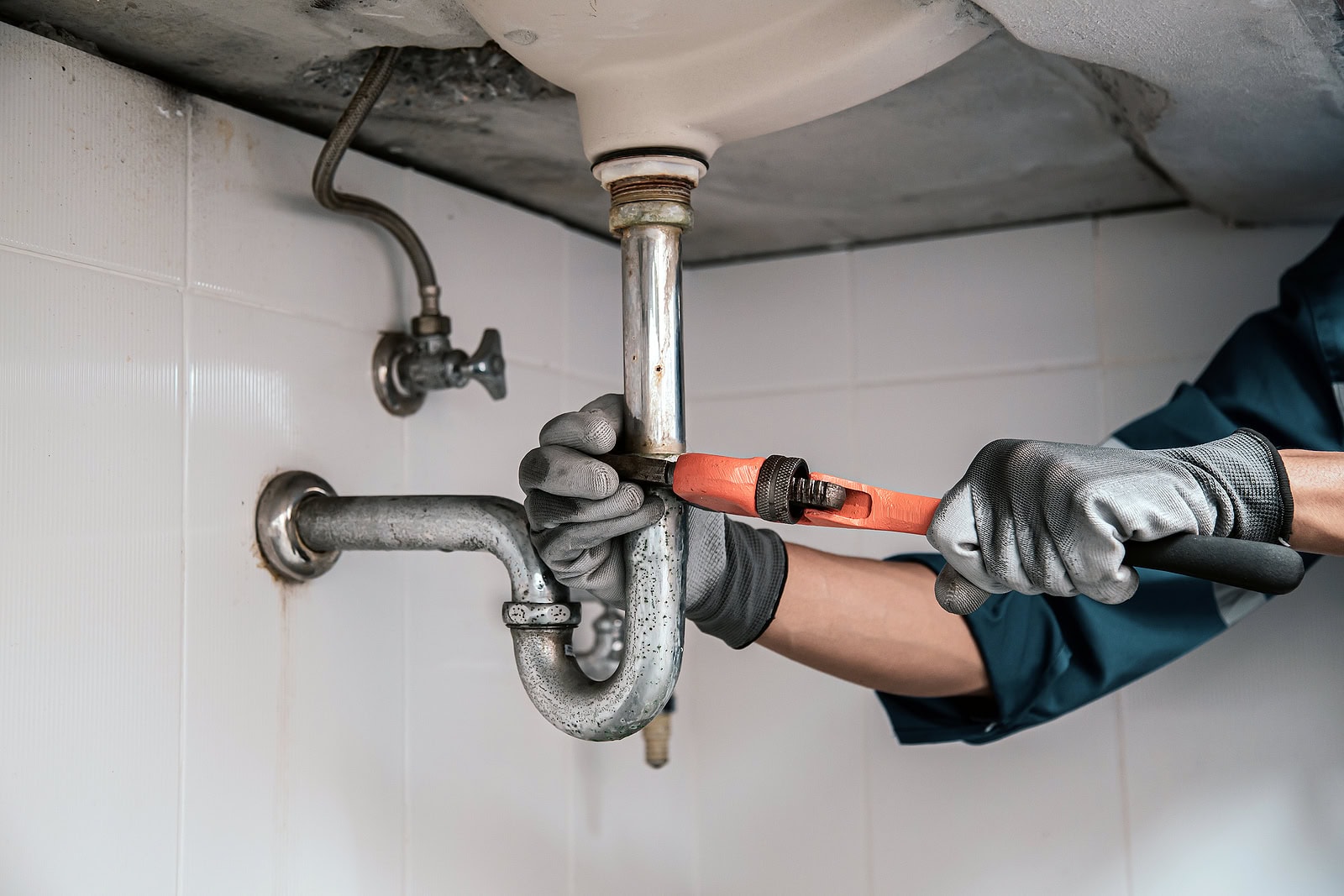 Technician plumber using a wrench to repair a water pipe under t